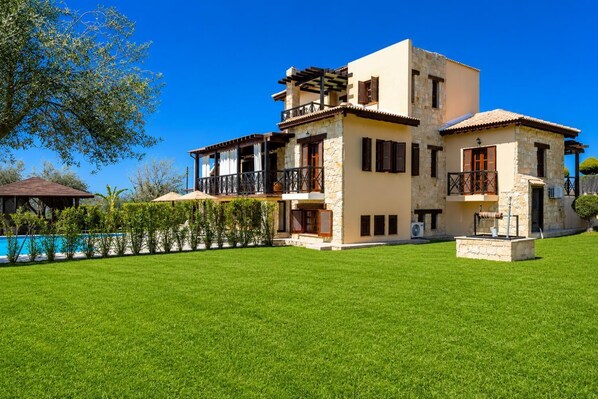Une maison à deux étages avec une piscine, une façade en pierre et une pelouse bien entretenue.