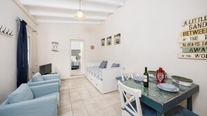 Un espacio habitable compacto con sofá, una mesa de comedor con sillas, cama y una pequeña cocina.