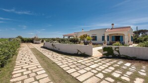 Un chemin pavé mène à une maison dont le toit est recouvert de tuiles et dont la façade est blanche.