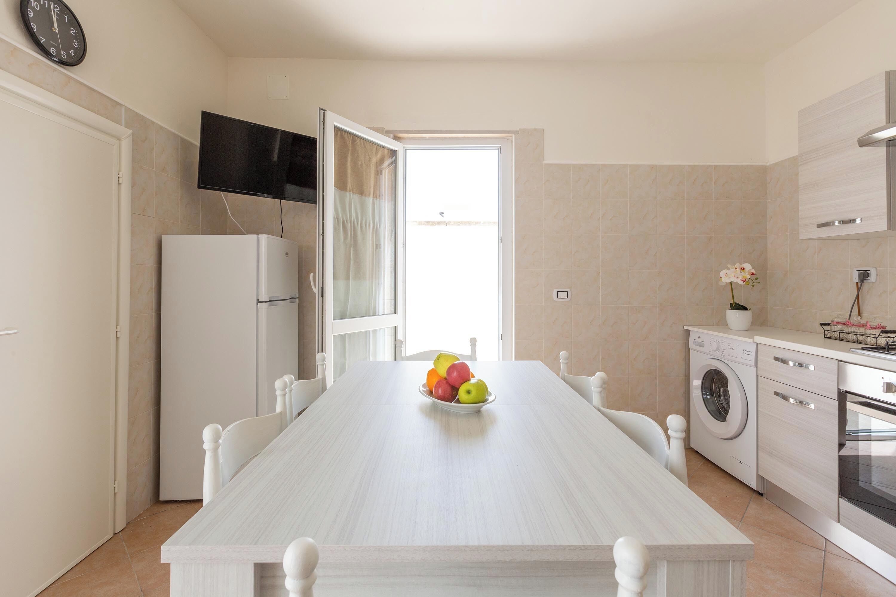 Eine moderne Küche mit Esstisch, Waschmaschine und einem an der Wand befestigten Fernseher.
