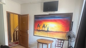Una camera d'albergo con due letti, un quadro raffigurante un paesaggio desertico, una televisione e una ventola.
