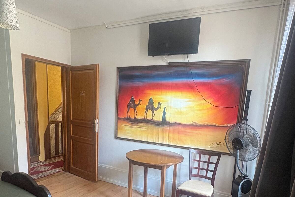 Quarto de hotel com duas camas, um quadro de uma paisagem desértica, uma televisão, um ventilador e uma escada que leva a outro cômodo.