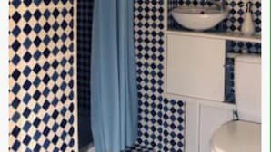 Un bagno con piastrelle a scacchi, una tenda blu per la doccia, un lavandino con specchio e un water bianco.