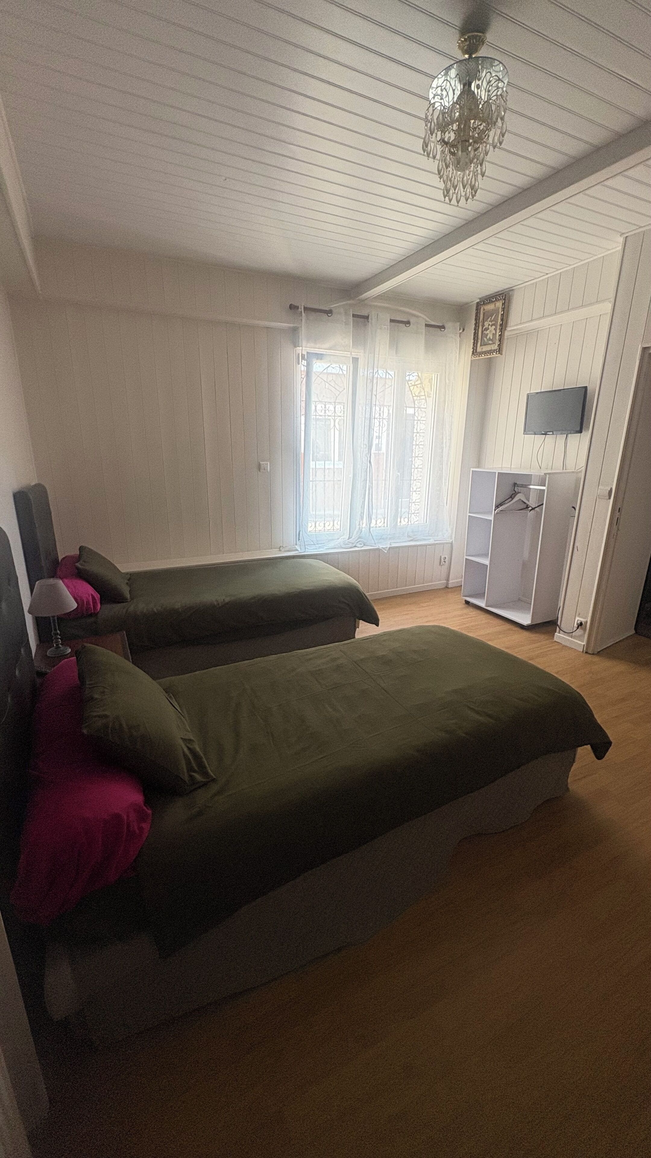 A room with two beds, a TV, a wardrobe, and a chandelier.