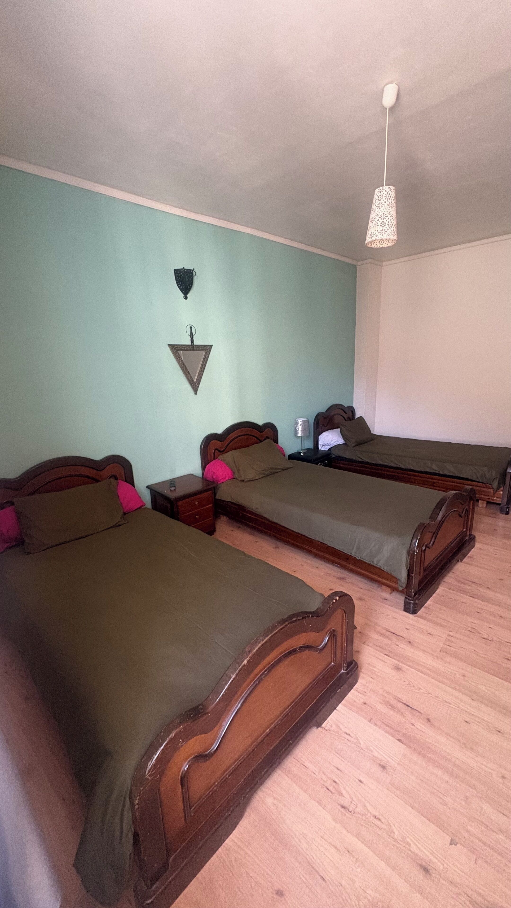 A room with three wooden beds, a wall-mounted light fixture, and a small wall decoration.