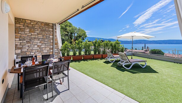 Un patio exterior con muro de piedra, una mesa con sillas y vista al mar.