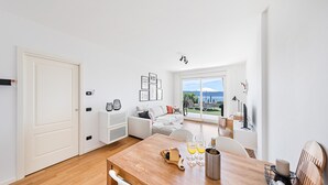 Una sala de estar moderna con comedor, muebles blancos y un amplio ventanal que ofrece vistas al exterior.