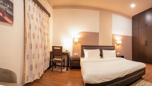 A hotel room with a bed, nightstands, a desk, a chair, and a wardrobe. - Firebrick Garnet House (Gurugram)