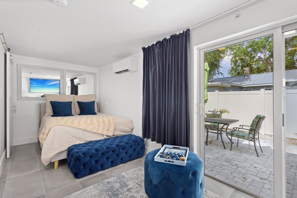 A bedroom with a bed, a bench, a table with chairs, and a sliding glass door leading to an outdoor area.