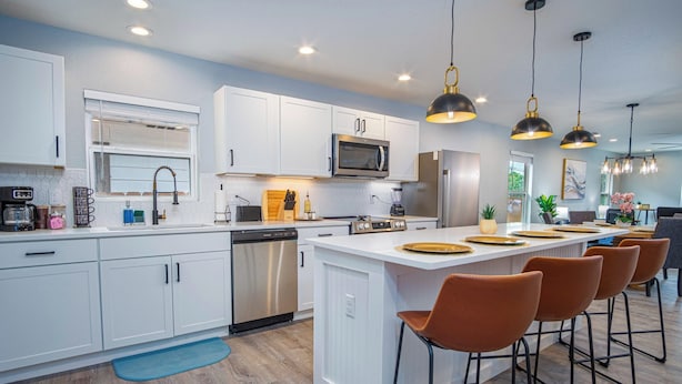 A modern kitchen with white cabinetry, stainless steel appliances, and a central island with bar stools.