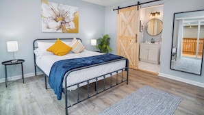 A bedroom with a bed, a large flower painting, a sliding door, a mirror, and a small plant.