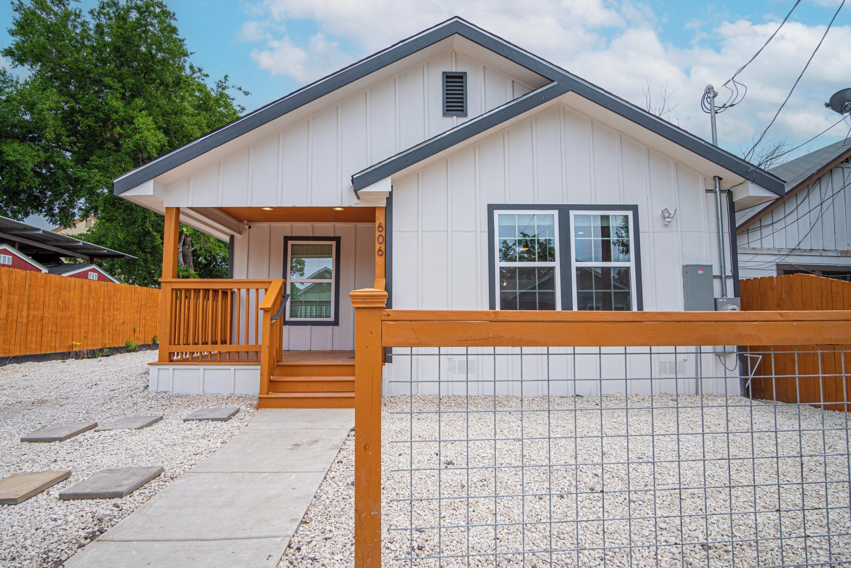 A single-story house with a front porch, a wooden fence, and a gravel driveway.