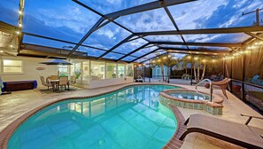 Une piscine entourée de parois en verre, un espace patio avec des chaises et une vue sur le ciel.