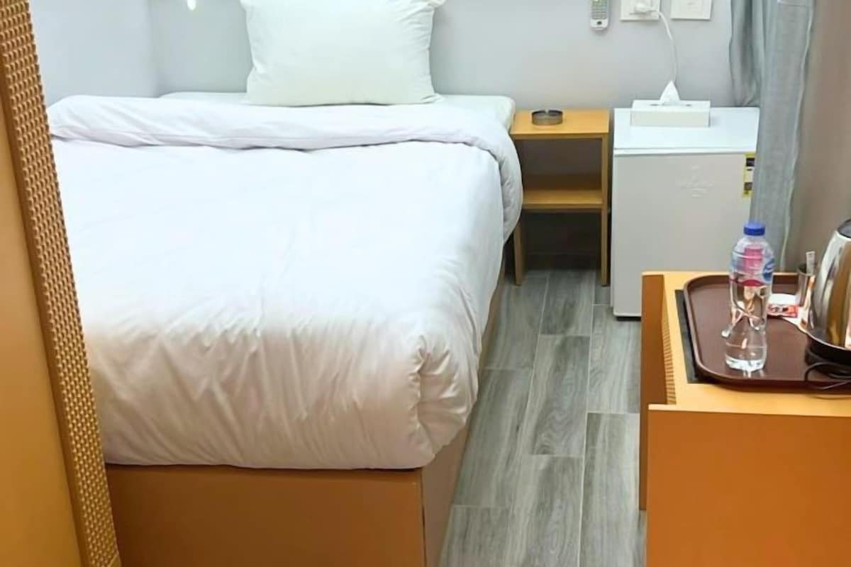 Una habitación de hotel con cama, mesita de noche, escritorio pequeño, botella de agua y caja de pañuelos.