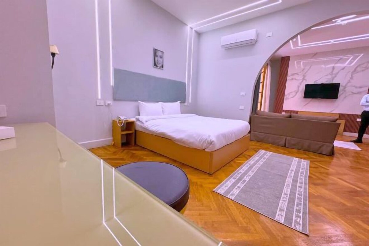 A modern hotel room with a bed, a sofa, a TV, and a wooden floor.