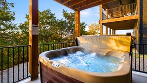 Un jacuzzi en una terraza de madera con vistas a árboles y un edificio al fondo.