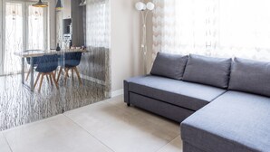 Ein modernes Wohnzimmer mit einem grauen Sofa, einem Esstisch mit Stühlen und einem Glastrennfeld mit Zweigdesign.
