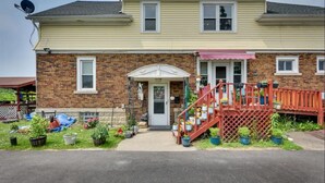 Une maison à deux étages avec une façade en briques, un porche à l’avant surmonté d’un auvent blanc et un escalier rouge menant à une terrasse.
