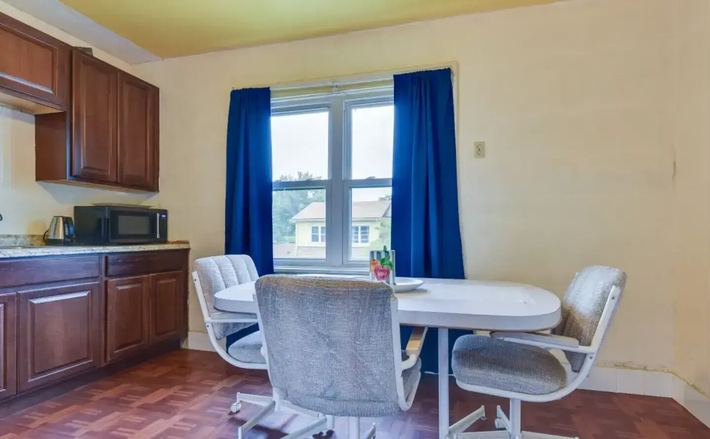 Una pequeña cocina con armarios de madera, un microondas y una mesa de comedor con dos sillas.