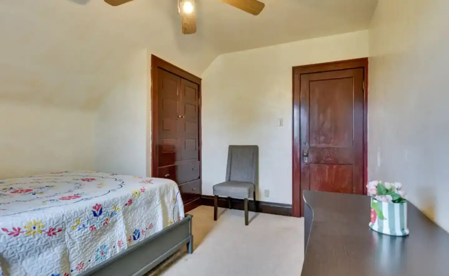 A bedroom with a bed, a chair, a table, and two doors.