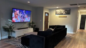 A modern living room with a flat-screen TV, a black sofa, a wooden floor, and a zebra-patterned rug. - Stylish house with pool close to strip (Las Vegas)