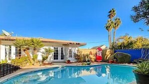 A swimming pool with a tiled edge, surrounded by palm trees and a house with a red door. - Stylish house with pool close to strip (Las Vegas)