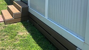 Una casa móvil con puerta corrediza de vidrio, unos escalones de madera y un patio cubierto de césped.