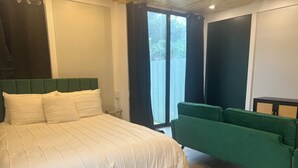 Un dormitorio con una cama grande, un sofá verde y vistas a la vegetación exterior.