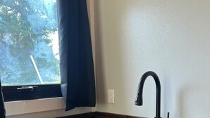 Una cocina con un lavamanos negro, encimera de madera, armarios blancos y una ventana que ofrece vistas a árboles.