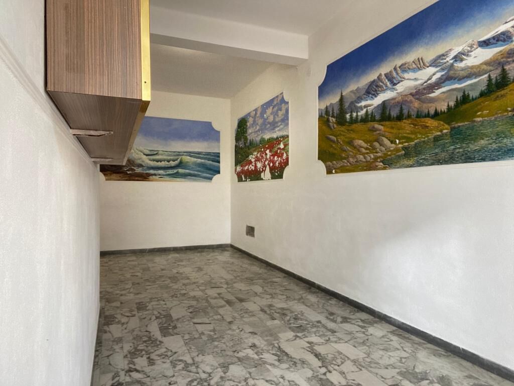 Un pasillo con piso de mármol y tres grandes cuadros de paisajes en las paredes.