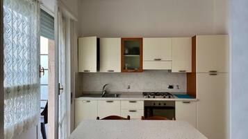 Une cuisine de taille réduite, équipée d’une cuisinière à gaz, d’un évier et de placards.