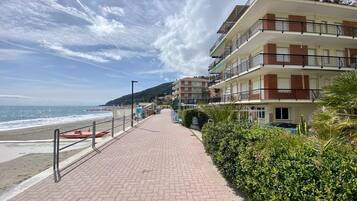 Eine Uferpromenade mit gepflastertem Gehweg, Gebäuden direkt am Strand und einem klaren Himmel.