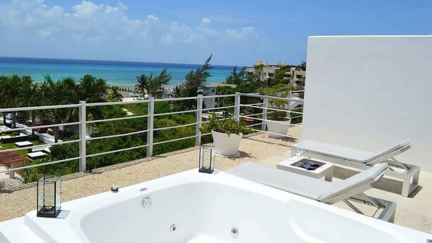 Un balcón con una bañera blanca, sillones de descanso y vista al océano y paisaje tropical.
