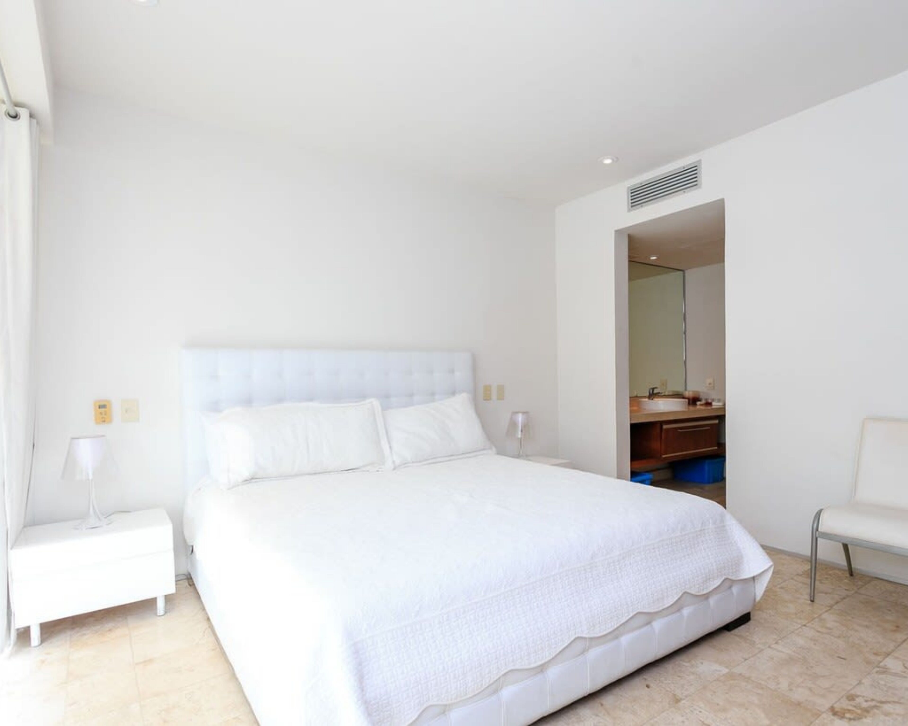 Un dormitorio con una cama grande, una mesita de noche y un baño visible a través de una puerta abierta.