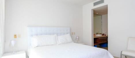Un dormitorio con una cama grande, una mesita de noche y un baño visible a través de una puerta abierta.