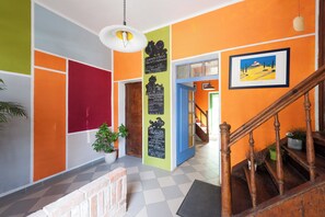 A brightly colored interior with a checkered floor, a wooden staircase, and a framed painting on the wall.