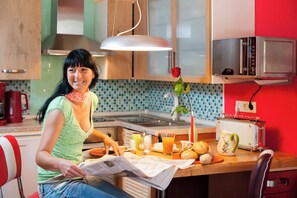 A kitchen with a woman reading a newspaper, a microwave, a toaster, and a rose on the counter.