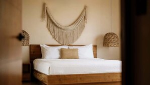 Un lit avec un cadre en bois, une décoration murale en macramé et deux lampes en fibres tressées.