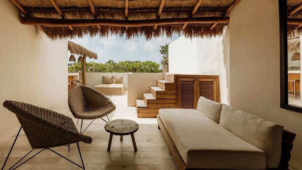 Un espace extérieur aménagé, abrité, avec un canapé, deux fauteuils en osier et une petite table ronde.