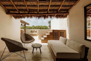A covered outdoor seating area with a sofa, two wicker chairs, and a small round table.