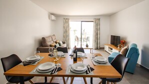 Uma sala de estar moderna com uma mesa de madeira posta para quatro pessoas, um sofá e uma televisão.