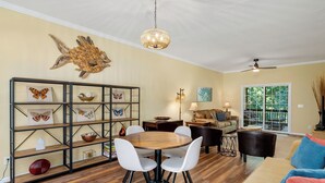 A spacious living room with a wooden dining table, white chairs, a black sofa, and a large wooden wall art piece. - Lakefront Treehouse Retreat Minutes from Clemson University! (Seneca)