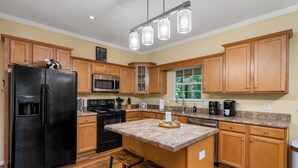 A modern kitchen with wooden cabinets, a black refrigerator, a granite countertop, and a hanging light fixture. - Lakefront Treehouse Retreat Minutes from Clemson University! (Seneca)
