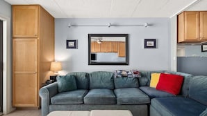 A living room with a sectional sofa, a small table, and wooden cabinets. - Oceanfront Studio-Sleeps4-Linens Incl-WiFi-Kitchen (Ocean City)