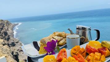 Bandeja de comida con alimentos y una cafetera, con vista a un paisaje costero.