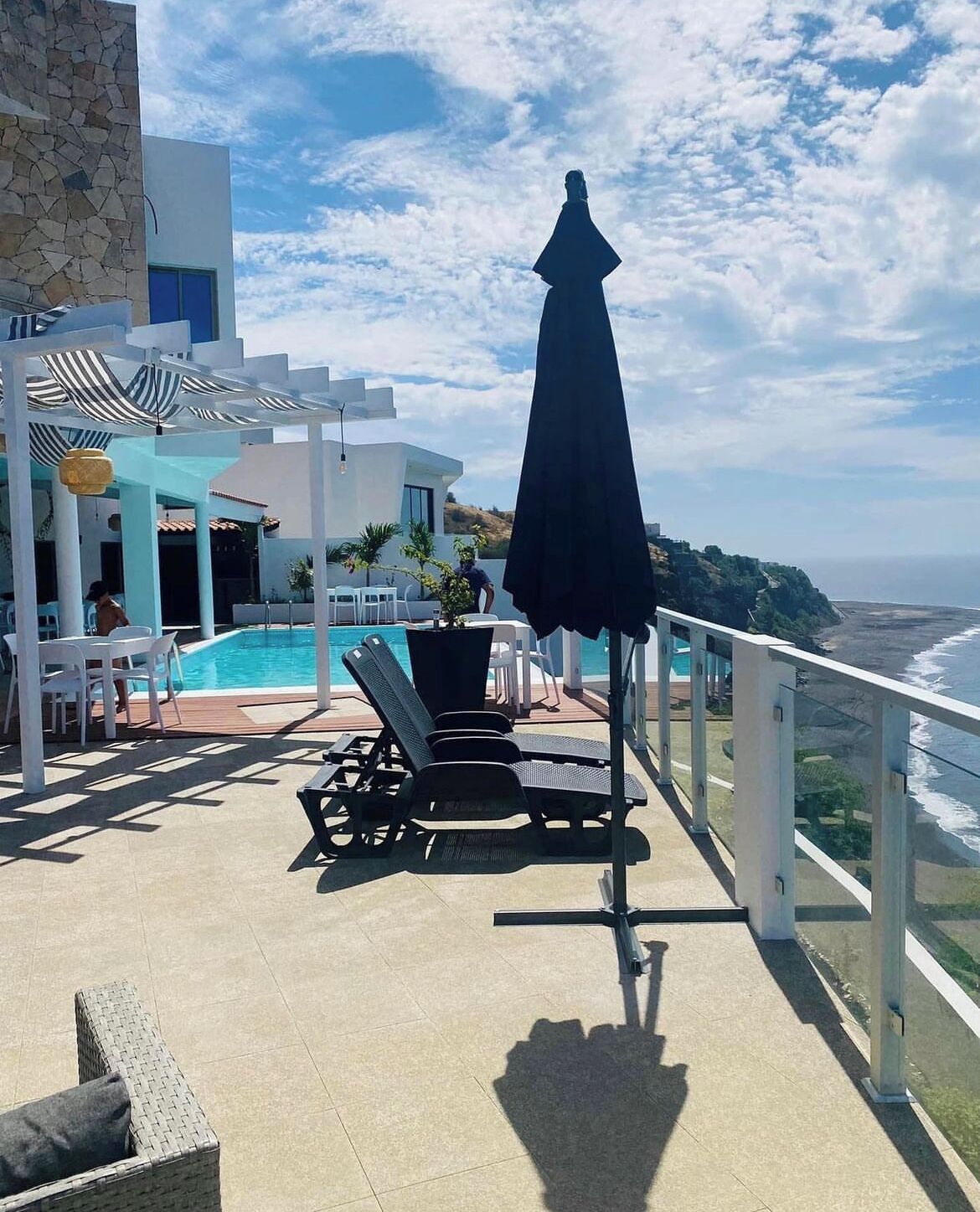 Un área de piscina en la azotea con sillones de descanso, una mesa y una sombrilla.
