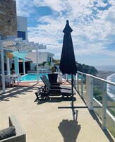 Un área de piscina en la azotea con sillones de descanso, una mesa y una sombrilla.