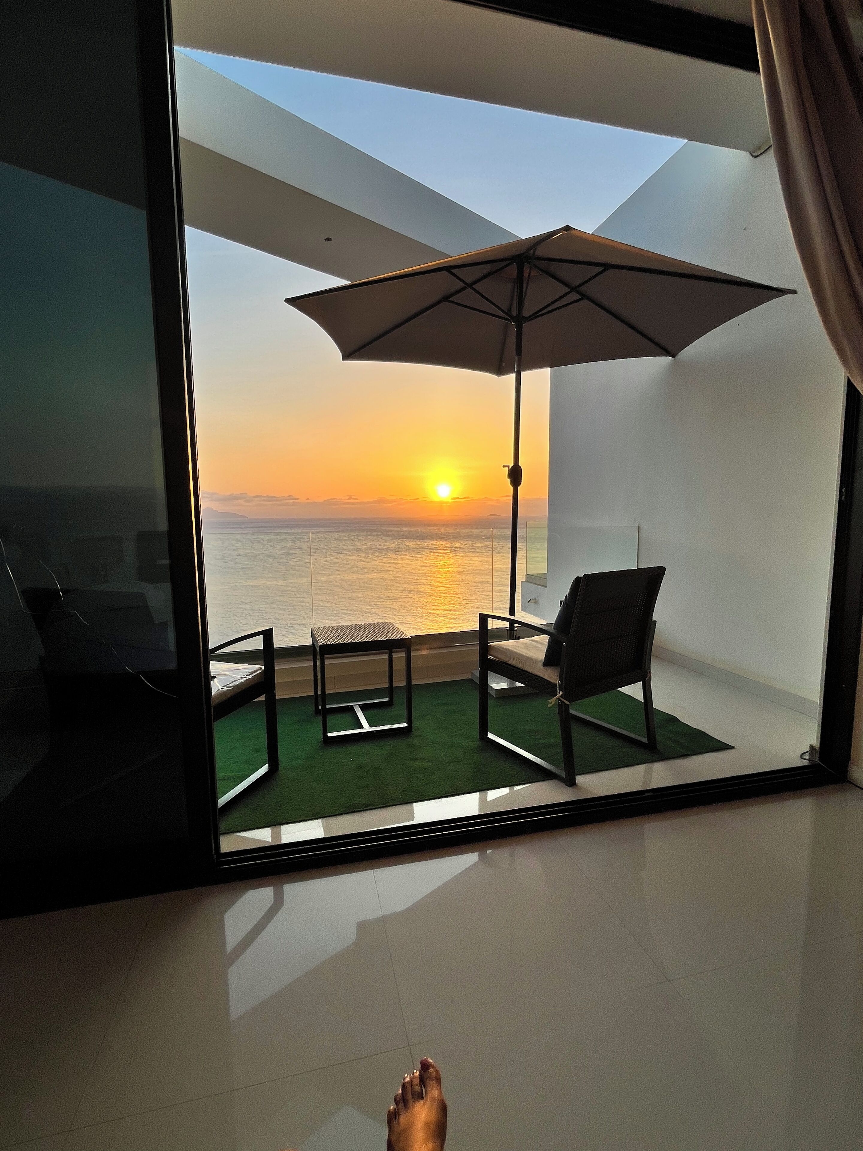 Una habitación con vistas a la puesta de sol sobre el océano, una pequeña mesa, una silla y un paraguas.