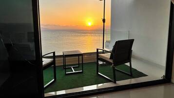 Una habitación con vistas a la puesta de sol sobre el océano, una pequeña mesa, una silla y un paraguas.
