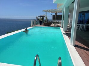 Una piscina con vistas al océano, un área de estar techada y un bar.